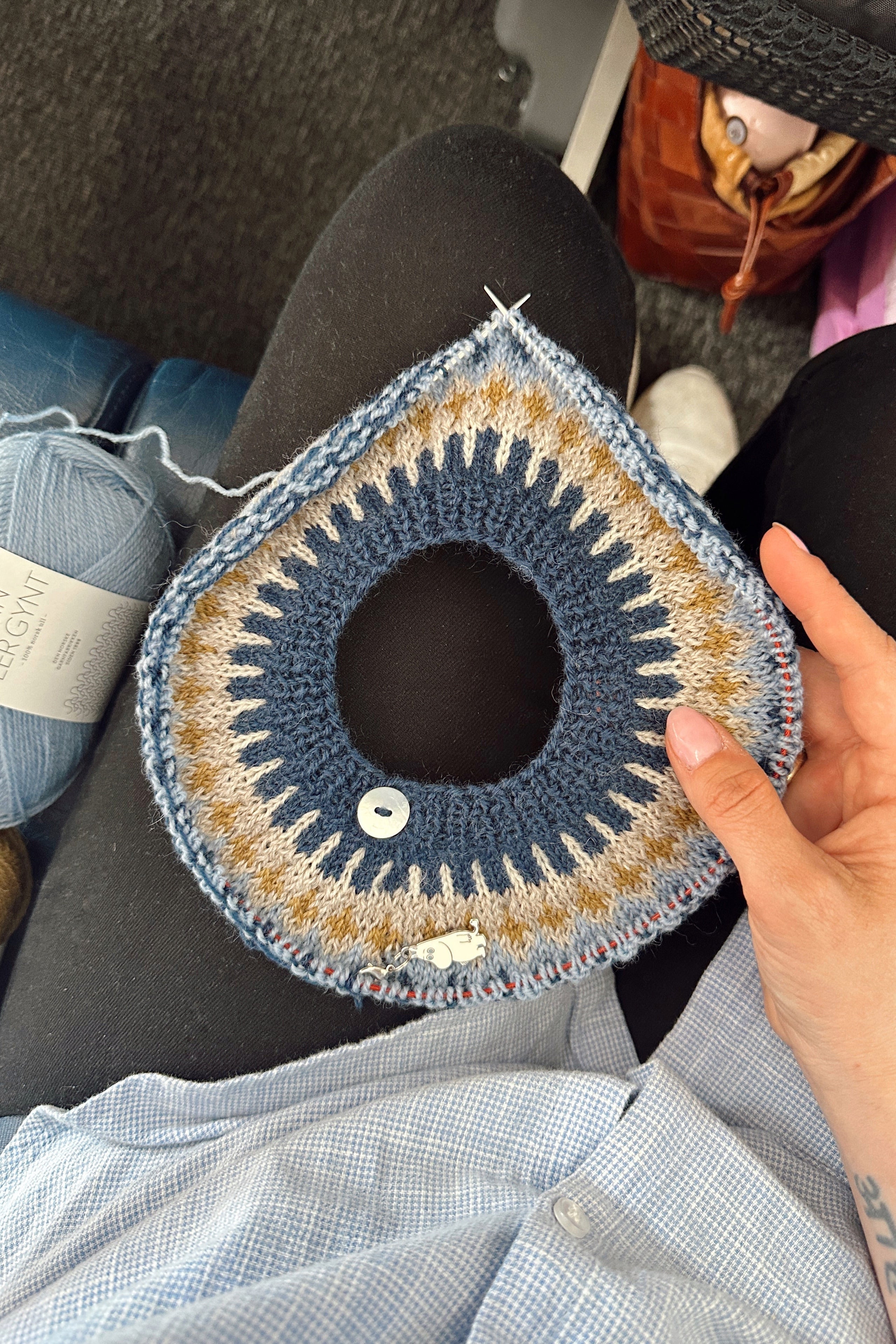 Hand holding a crocheted circular item with yarn and a hook on a lap.
